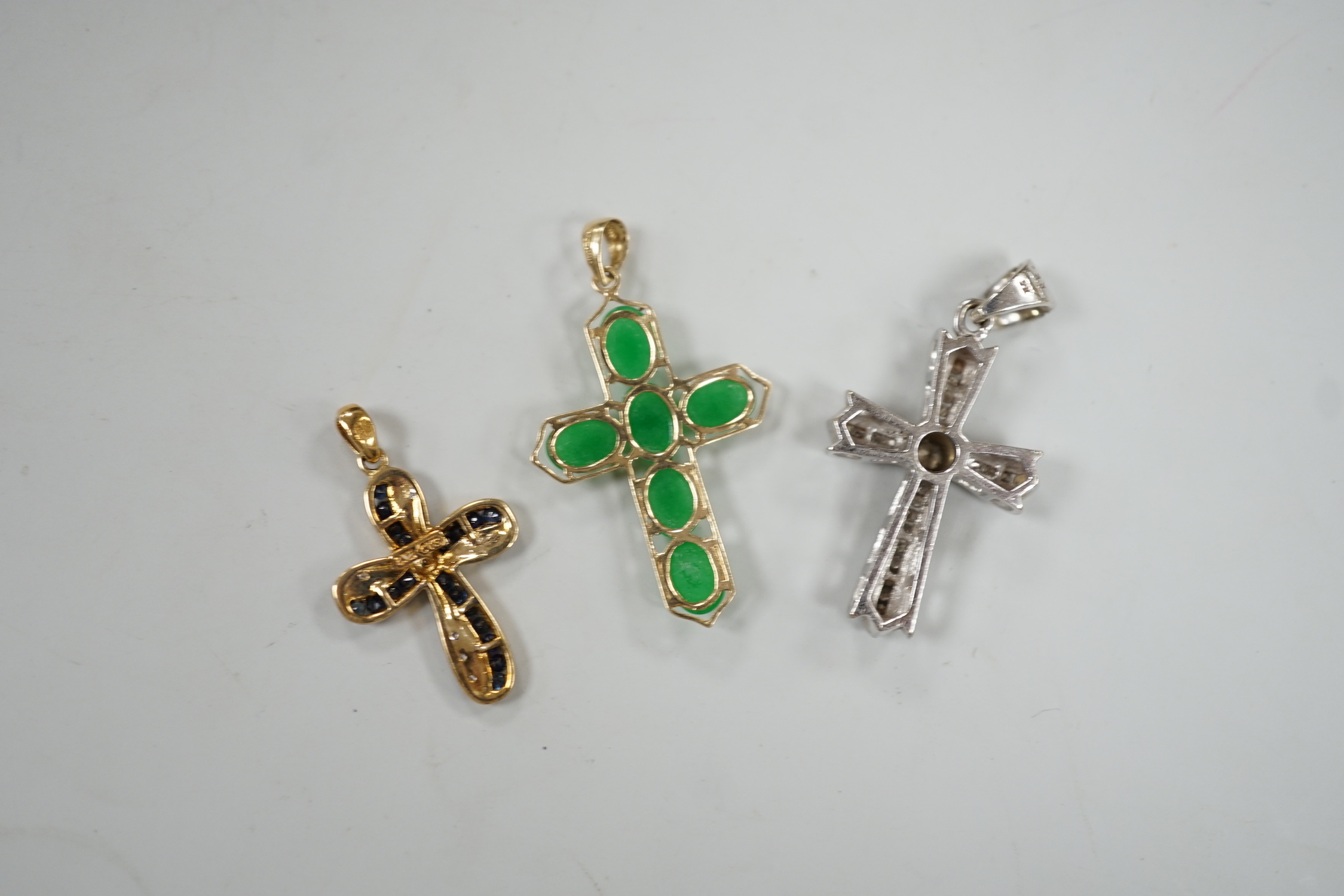 A modern 9ct white gold and diamond cluster set cross pendant, 27mm, a modern 9ct gold, sapphire and diamond chip set cross pendant, gross 7.4 grams and a 14ct gold and six stone cabochon jade set cross pendant, gross we